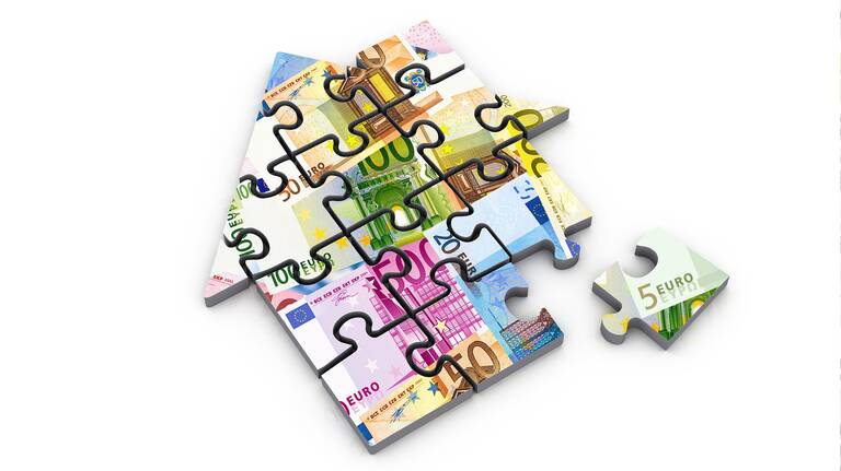Puzzlestücke mit Werten von Geldscheinen ergeben das Bild eines Hauses (Symbol für Miete)