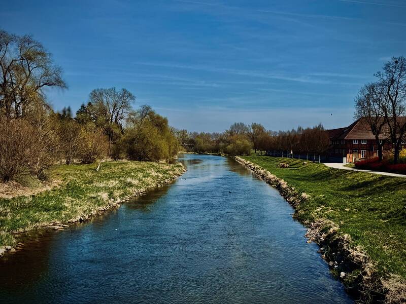 Blick auf die Donau von der Fußgängerbrücke, gesäumt jeweils von grünem Ufer und Bäumen