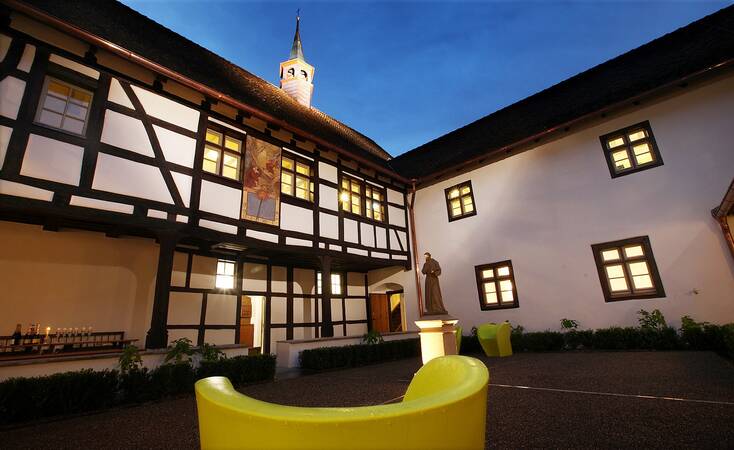Innenhof des Kapuzinerklosters bei Nacht mit Fachwerkfassaden und Türmchen im Hintergrund