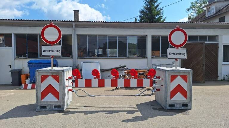 Vor einem Gebäude steht eine rot-weiße Straßensperre mit "Veranstaltung"-Schildern.