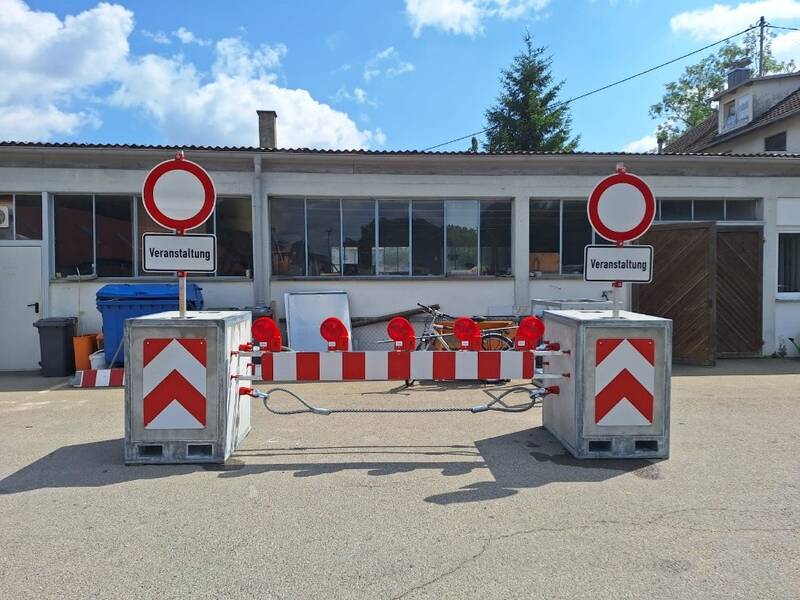 Vor einem Gebäude steht eine rot-weiße Straßensperre mit "Veranstaltung"-Schildern.