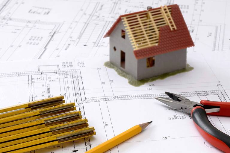 Modell eines Hauses sowie Bleistifte auf einem Gebäudeplan (Beispielbild für Bauen)