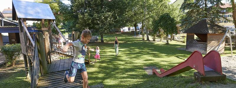 Spielendes Kind inmitten der Spielgeräte im begrünten Außenbereich des Kindergartens Grüningen