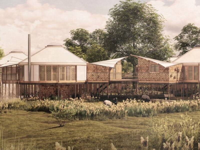 Ein modernes Gebäude-Ensemble mit Holz- und Glaselementen steht auf Stelzen in einer grünen, von Gras und Bäumen umgebenen Landschaft.
